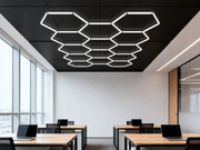 Hexagon HEXO 14-GRID LED-valosarja asennettuna toimiston mustaan kattoon muodostaen kennokuvion, alla puiset ty&ouml;p&ouml;yd&auml;t