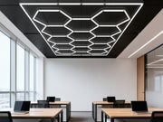 Hexagon HEXO 14-GRID LED-valosarja mustassa kehyksess&auml; asennettuna toimistotilan kattoon, taustalla puiset ty&ouml;p&ouml;yd&auml;t ja kannettavat tietokoneet