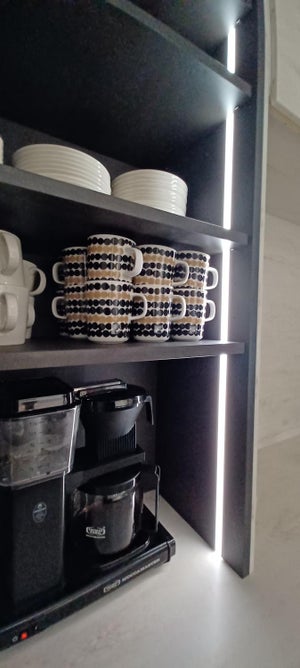 Musta profiili upotettuna mustaan kaapiston runkoon. Sivulta tuleva valo valaisee kauniisti kaapin esineet ja antaa työskentelyvaloa.